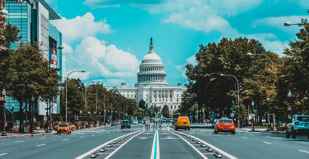 View of the U.S. Capitol building in Washington D.C. with its large white dome and columns under a clear blue sky.