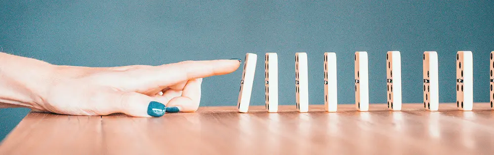 A closeup of a woman s finger gently pushing the first in a row of standing dominoes symbolizes the start of a chain reaction and represents the domino effect with potentially negative consequences