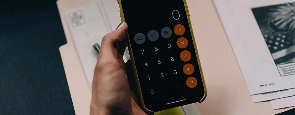 A hand holding an iPhone with the Calculator app open displaying a zero on the screen symbolizing a missed budget or financial shortfall