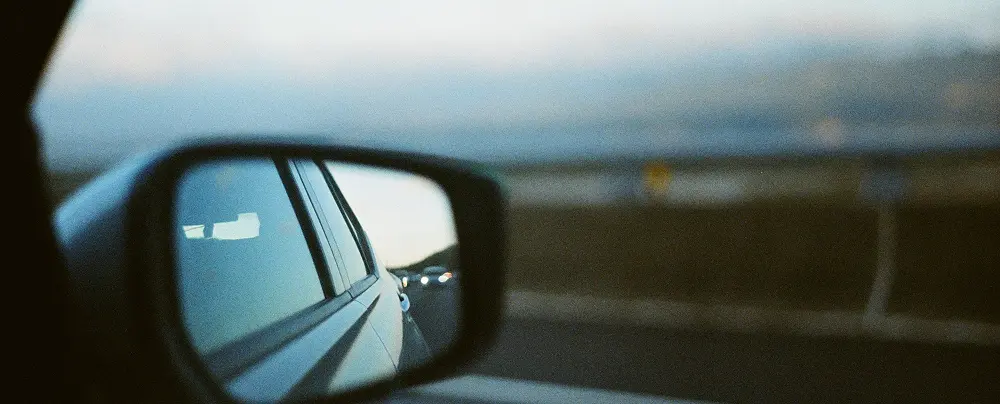 Close-up of a car s side mirror with part of another vehicle just outside the mirror s view suggesting the presence of a blind spot