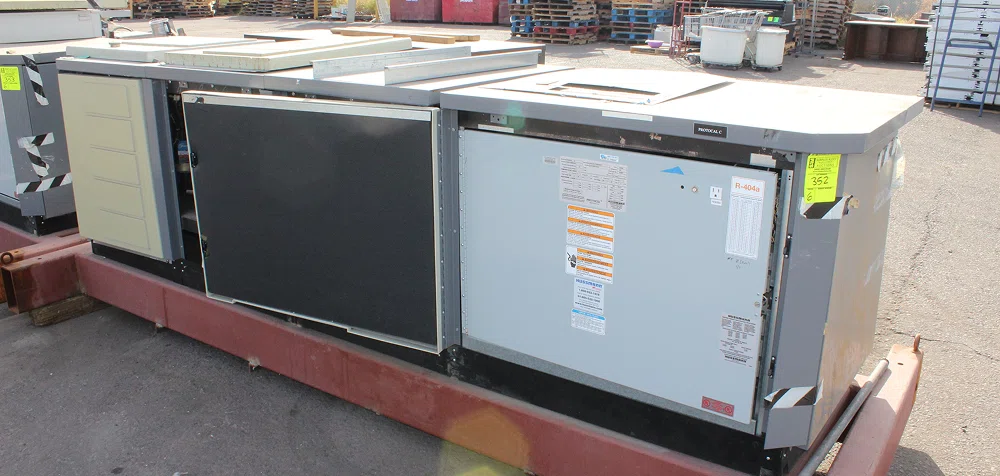 Large commercial rooftop HVAC unit labeled with R-404A refrigerant, situated outdoors on a metal skid in an industrial storage yard with pallets and equipment in the background
