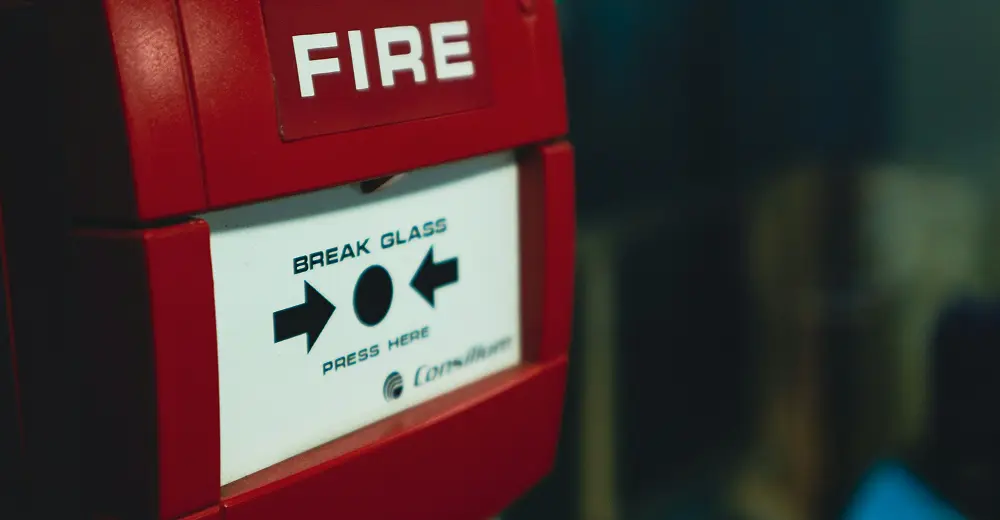 Red emergency fire alarm with the words Fire – Break Glass – Press Here displayed on the front panel