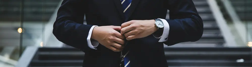Close-up of a man’s arms in a corporate suit, wearing a tie and watch, representing business and finance