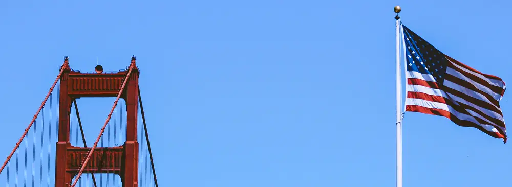 Cropped view of the San Francisco Bridge in California with a U.S. flag against a clear blue sky