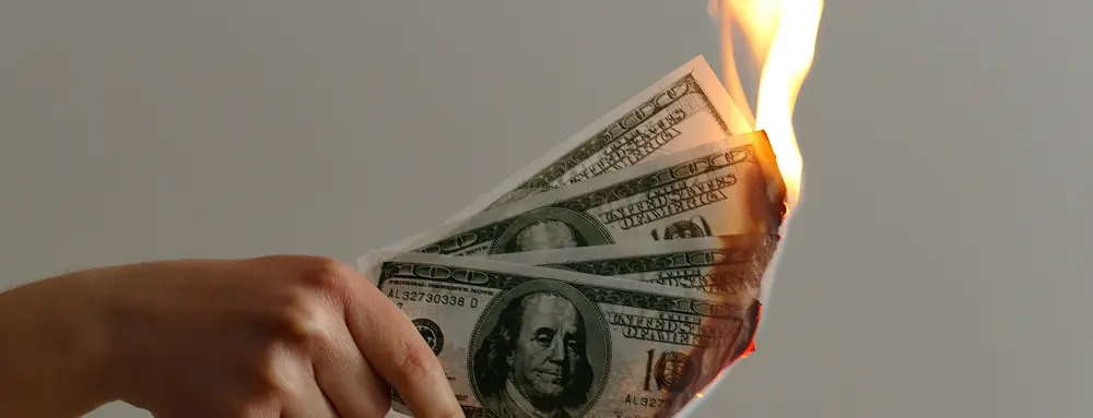 Female hand holding burning one-hundred-dollar bills, symbolizing a budget going up in flames