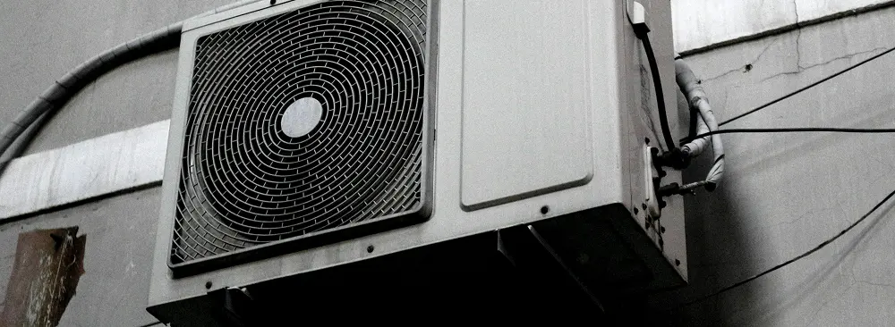 Outdoor unit of a heat pump or air conditioning system mounted on a building wall, with visible wiring and piping