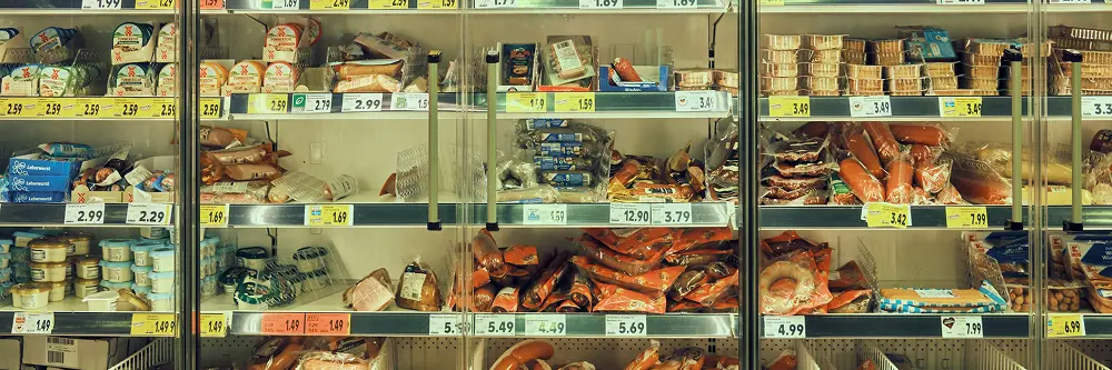 Refrigerated supermarket shelves stocked with packaged meats, sausages, and dairy products, each labeled with price tags