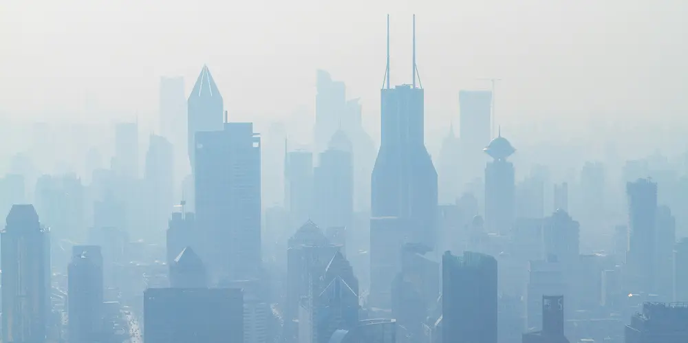 Silhouette of buildings shrouded in thick fog and haze, suggesting heavy air pollution.