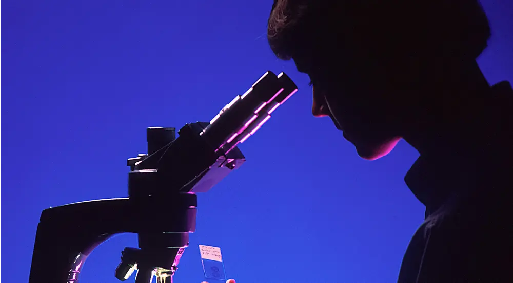 Woman looking into a microscope in a blue and black image
