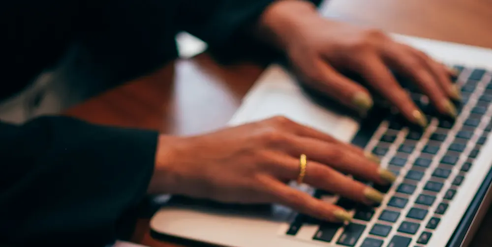 close-up of an elegant woman’s hands typing on a dark keyboard