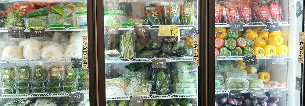 Interior of a refrigerated supermarket with neatly arranged vegetables on display in open coolers