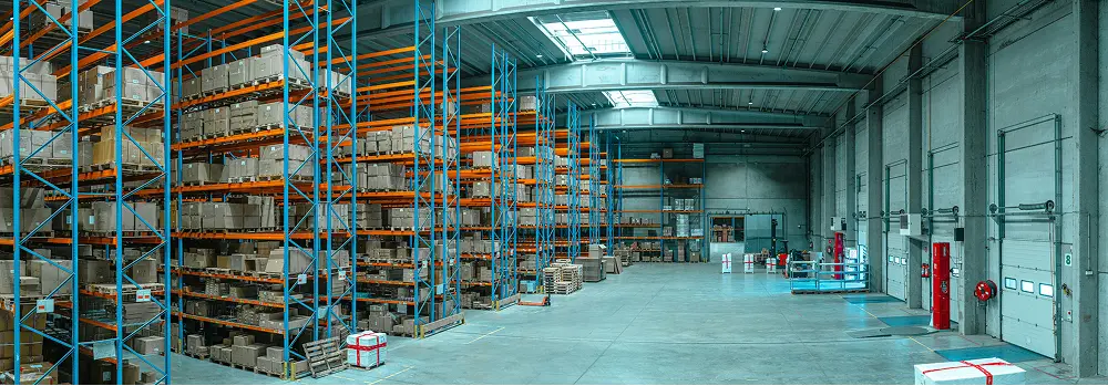 Large warehouse interior with tall shelves filled with boxes and packages, and open space for loading and unloading