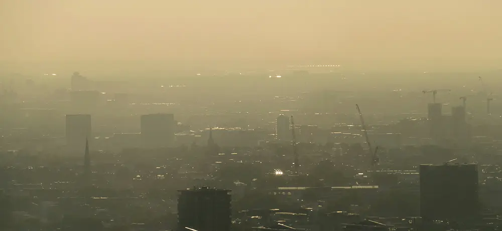 City skyline covered in thick smog, with buildings and cranes barely visible through the haze