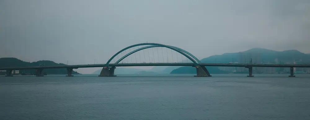 A long bridge over water, with a city in the background, cloudy weather