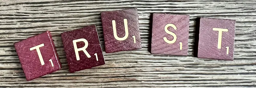 Dark red Scrabble tiles spelling TRUST on a wooden table
