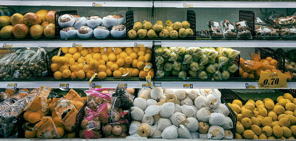 Refrigerated grocery store shelves stocked with various packaged fruits, including lemons, pears, and oranges