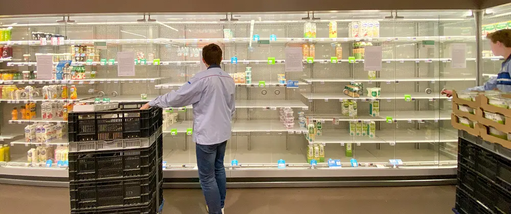 Two men stocking items from crates onto nearly empty refrigerated shelves