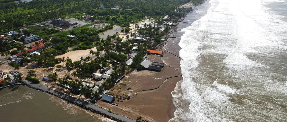 Aerial view of a beach with constructions near the shoreline and ocean waves crashing in, symbolizing vulnerability to storms and climate change