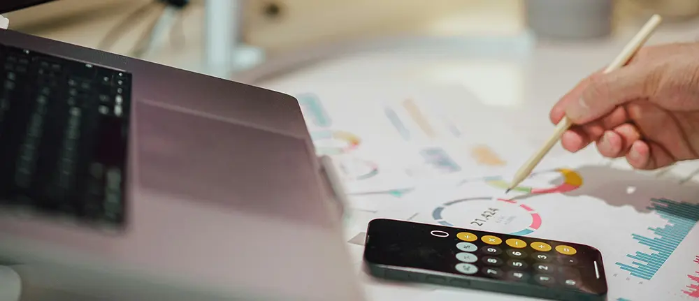 Person using a pen, laptop and calculator on printed reports