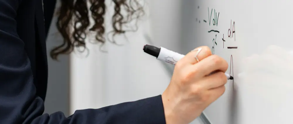 Woman writing on a whiteboard, working through formulas