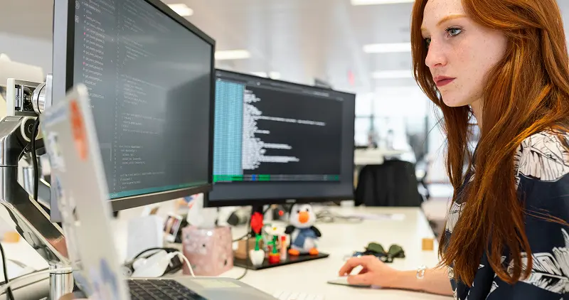 A young woman focused on her studies while working with several monitors
