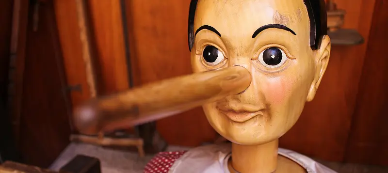 A hand-carved wooden Pinocchio figurine featuring his iconic long nose and articulated joints symbolizing the lies