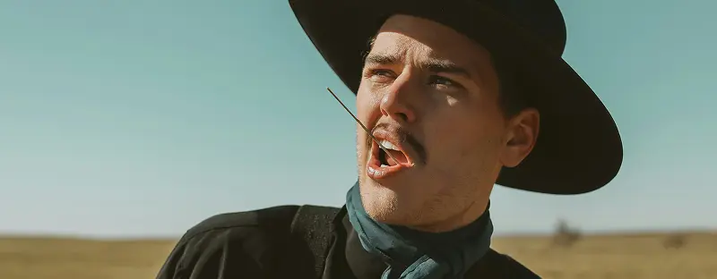 A shot of a young cowboy with a straw in his mouth gazing toward a clear blue sky