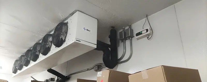 AKO leak detector mounted on the wall.
Indoor shot of a walk-in freezer featuring a white Russell evaporator unit with six fans. Cardboard boxes are stacked in the foreground.
