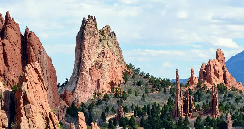 Rocky mountain peaks tower over a valley of evergreen trees in a Colorado national park with a cloudy sky above